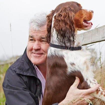 Mann kniet mit Hund vor Zaun